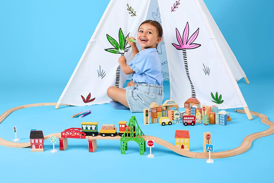 A kid smiling while sitting at the hem of a Chad Valley toy tent while surrounded by other toys.